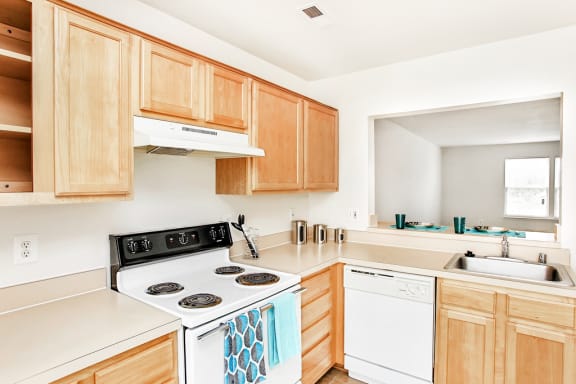 Kitchen with tile floors, white appliances, and wood cabinets. Living room in background with large window.