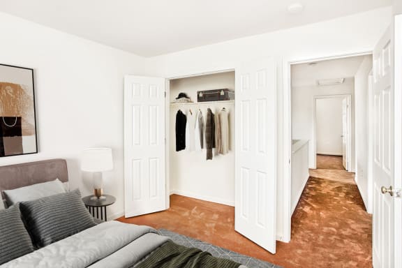 Virtually staged bedroom. Carpeted bedroom with grey and tan accent bed/artwork. Closet in background.