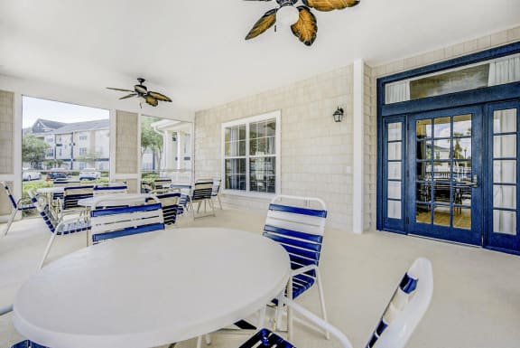 Inward facing view on the screened-in lanai featuring ceiling fans, outdoor tables and chairs and entrance door into clubhouse
