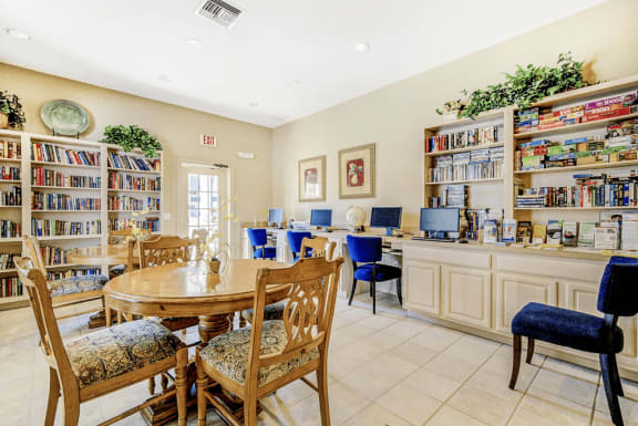 Library and media room containing tables and chairs filled with books, board games, movies, puzzles, seated computer desks and printer.