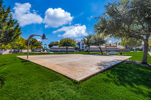 A basketball court is surrounded by trees and grass.