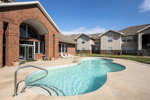 Leasing Office Exterior with Swimming Pool and Sun Deck with Lounge Chairs and Building Exteriors Behind Fence
