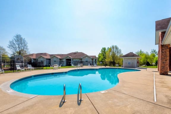 Swimming Pool with Sundeck and Lounge Chairs with  Treeline and Building Exteriors in the Background