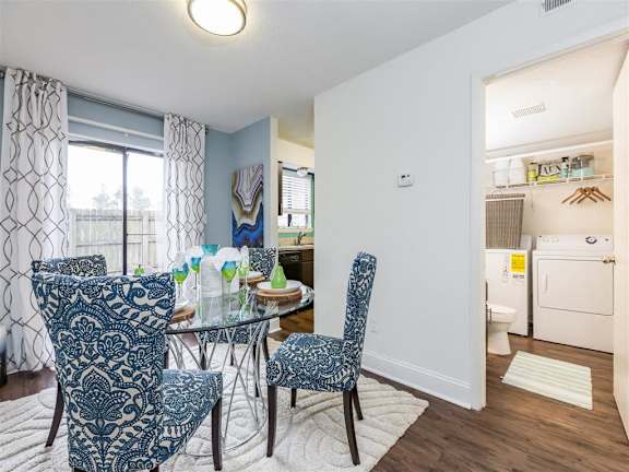 Furnished Model Dining Room with Glass Dining Table and Chairs on Area Rug Next to Utility CLoset with Washer and Dryer at Regency Park Apartment Homes, Raleigh, North Carolina