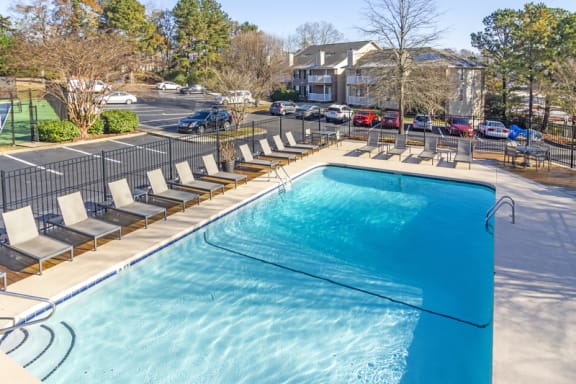 a swimming pool with chaise lounge chairs and a parking lot in the background