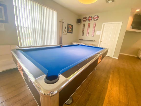 Blue pool table inside the leasing office on wood style flooring with tv mounted in the background