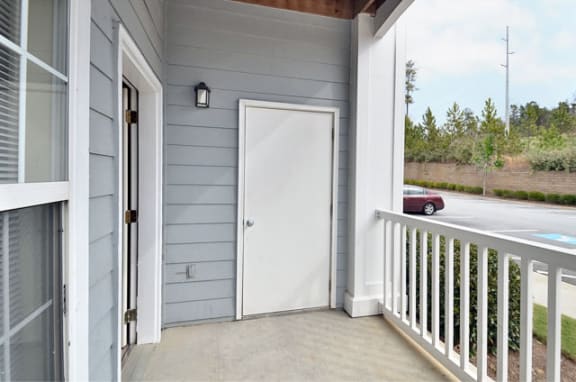 Apartment patio with concrete flooring and white railing. A private storage unit is off of the patio.