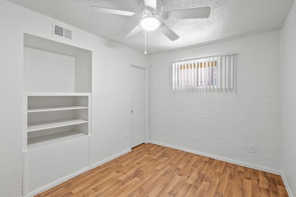 a bedroom with hardwood floors and a ceiling fan, as well as built-in shelves