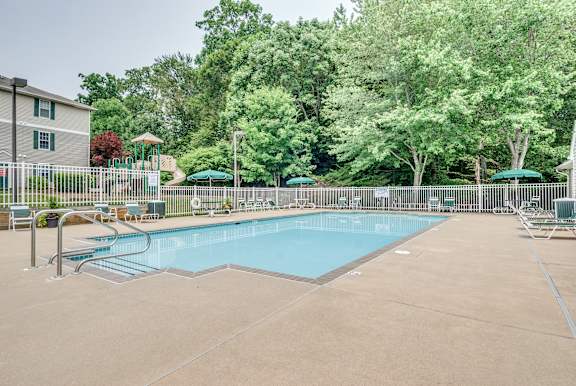 A large swimming pool surrounded by trees and a playground.