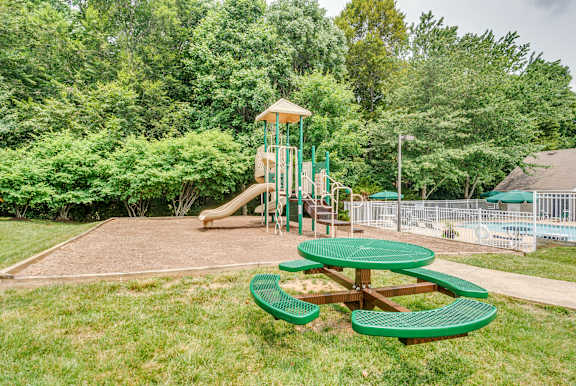 A playground with a green slide and picnic tables.