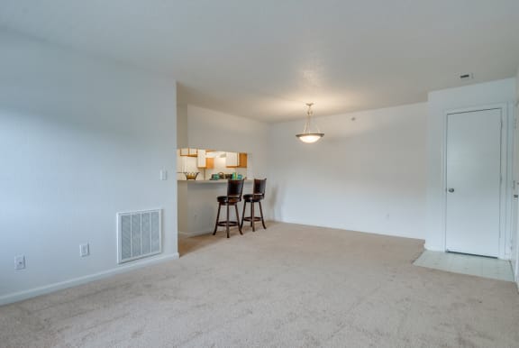 The living and dining room has carpet with linoleum flooring in the entry. There is breakfast bar that opens to the kitchen. This mini model is furnished with two barstools positioned at the breakfast bar.