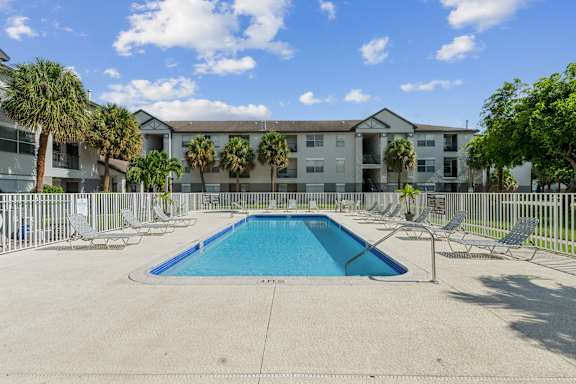 A swimming pool in front of a building with palm trees.