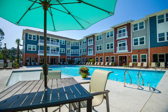 an outdoor pool with a table and chairs in front of an apartment building