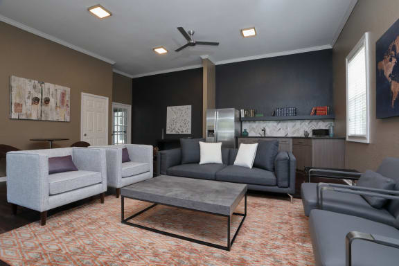 The Resident Lounge is a big room with a contemporary design. The far wall has a small Clubhouse Kitchen. Two light cloth chairs are on the left in front of a coffee table with a dark sofa on the far side.