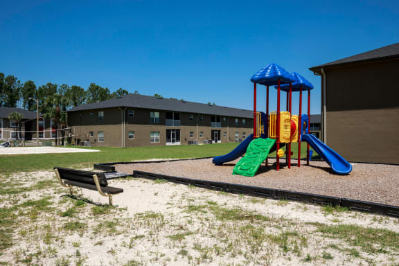 Playground jungle gym and playground slides in a bed of mulch with trees, and sand volleyball court in the background