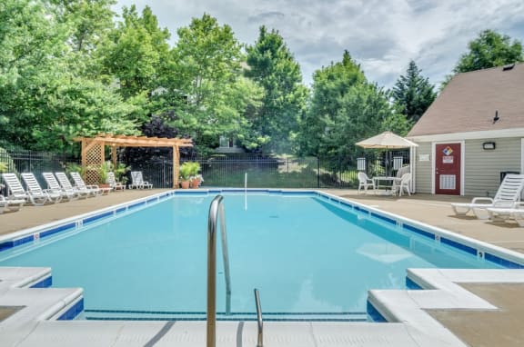 Swimming pool with sundeck, lounge chairs, pergola, umbrellas and potted plants surrounds by building exteriors and mature trees