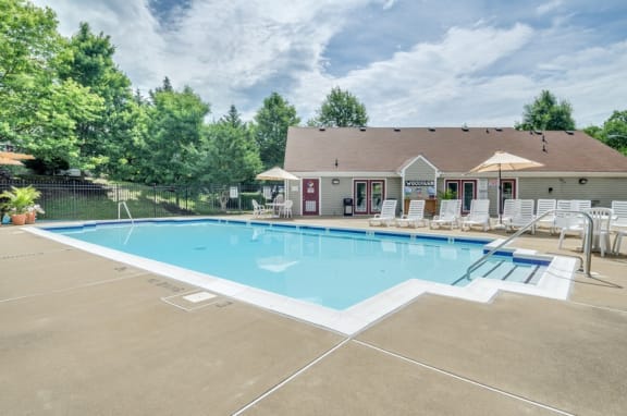 Swimming pool with sundeck, lounge chairs, pergola and potted plants surrounds by building exteriors and mature trees