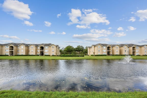 a pond with a fountain in front of a row of apartment buildings
