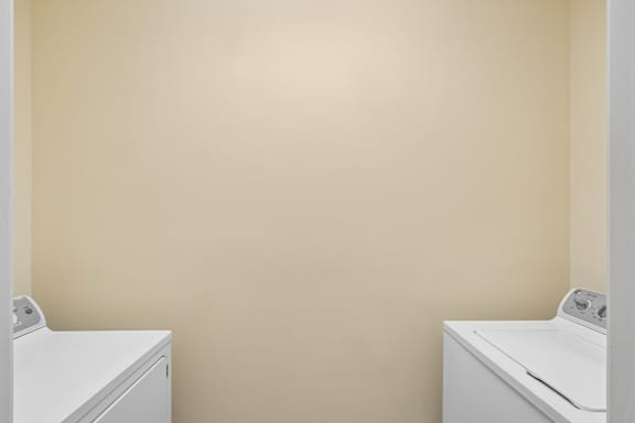 Two white washing machines in a room with beige walls.