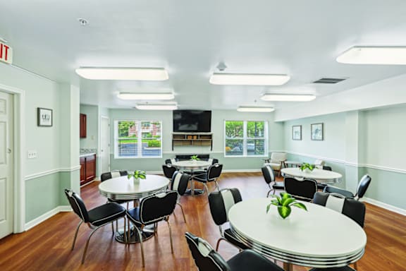 A white table with a green plant on it is surrounded by black chairs in a room with a white ceiling and a door with a red exit sign above it.
