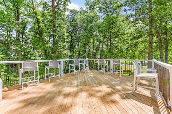 A wooden deck with white chairs and a railing overlooking a forest.
