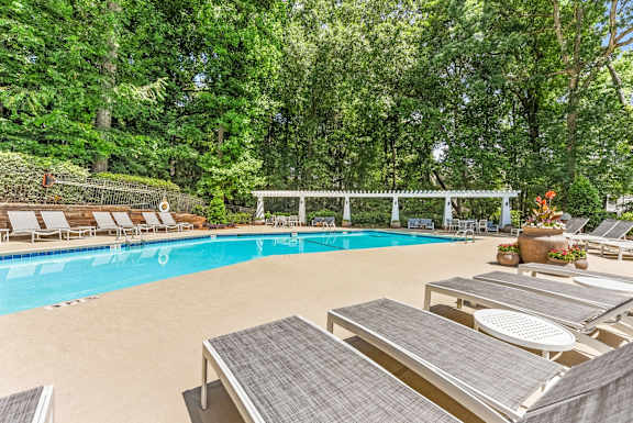A pool surrounded by trees and lounge chairs.