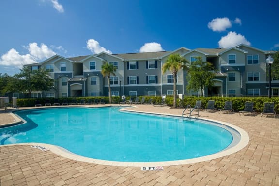 Swimming pool with lounge seating, surrounded by native landscaping and apartment building exterior in the background