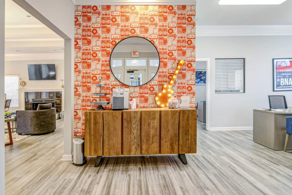 a resident lobby with an orange brick wall with a round mirror and a wooden desk with a
