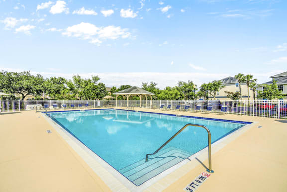 Swimming pool with lounge seating surrounded by native landscape and grill pavilion in background