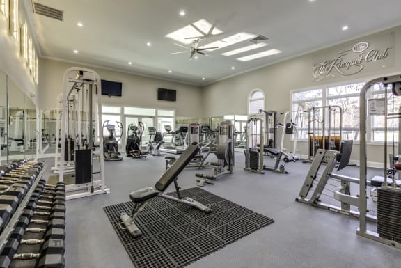a spacious fitness center with cardio machines, free weights and strengthening machines. A mirrored wall with 2 tvs and ceiling fans.
