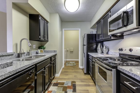 Gally style kitchen with stainless steel appliances, undermount sink, granite counters, and wood style flooring leading to the laundry room.