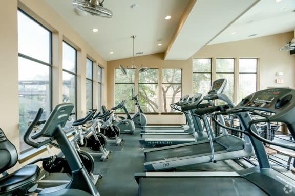 a gym with cardio equipment and large windows