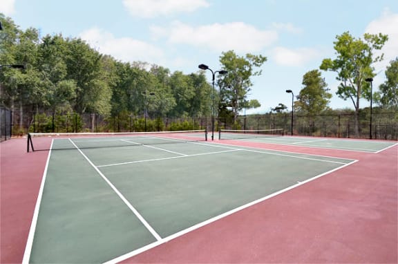Community tennis courts with a red base and green courts with lines. A black fence surrounds the courts.
