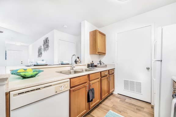 Kitchen with breakfast bar, double basin sink, wood cabinetry, and a dishwasher across from a white refrigerator and electric stove. A door in the background opens to the laundry room.