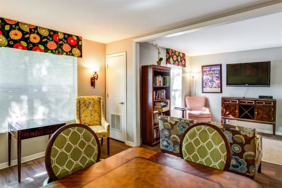 Model Floor Plan with Wooden Dining Room Table Green and White Chairs Book Shelf Couch TV and Entertainment Center