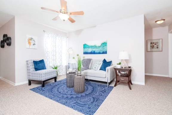 furnished living room model with couch, ceiling fan, and area rug.