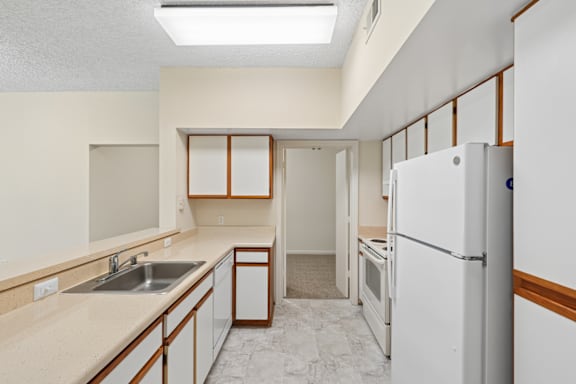 A kitchen with a white refrigerator, sink, and cabinets.