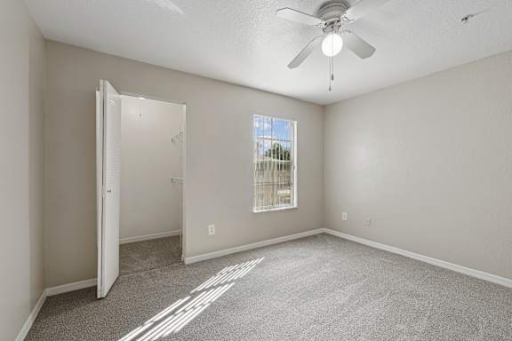 A room with a ceiling fan and a window with bars.