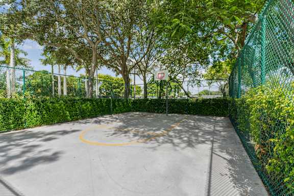 A basketball court surrounded by a green fence and trees.