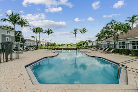 A large outdoor swimming pool surrounded by palm trees and lounge chairs.