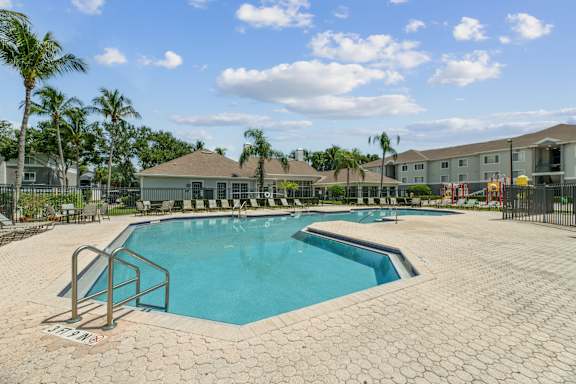 A large swimming pool surrounded by a brick patio and palm trees.