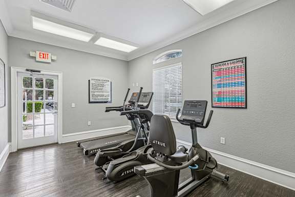 A gym with treadmills and a red exit sign.