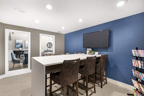A room with a white desk and brown chairs with a blue wall and a black television.