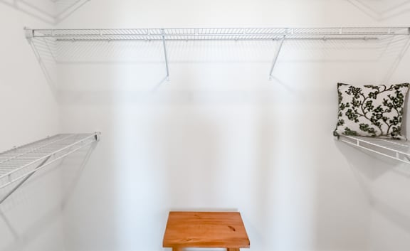 a white closet with two shelves and a pillow on a bench