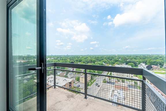 A balcony with a view of a parking lot and trees.