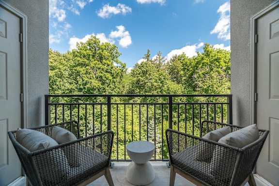 Two chairs are on a balcony with a view of trees.