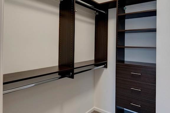 A white wall with a brown shelf and a black drawer.