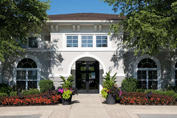 A white building with a black door and windows surrounded by plants.