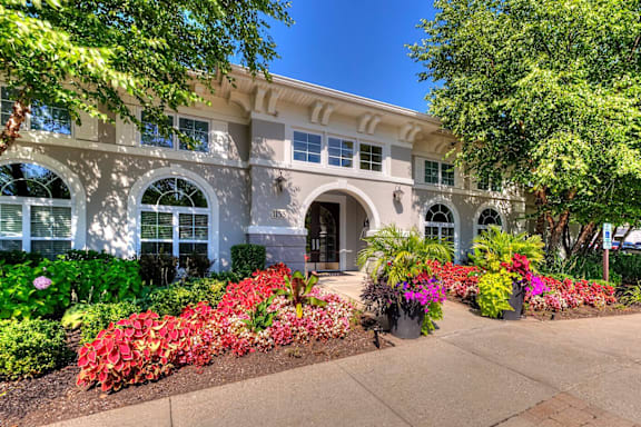 A white building with a large arched doorway and windows flanked by flower beds.