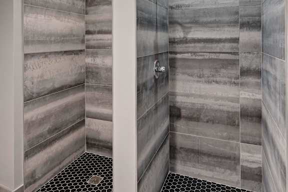 A bathroom with a tiled shower and a black and white floor.